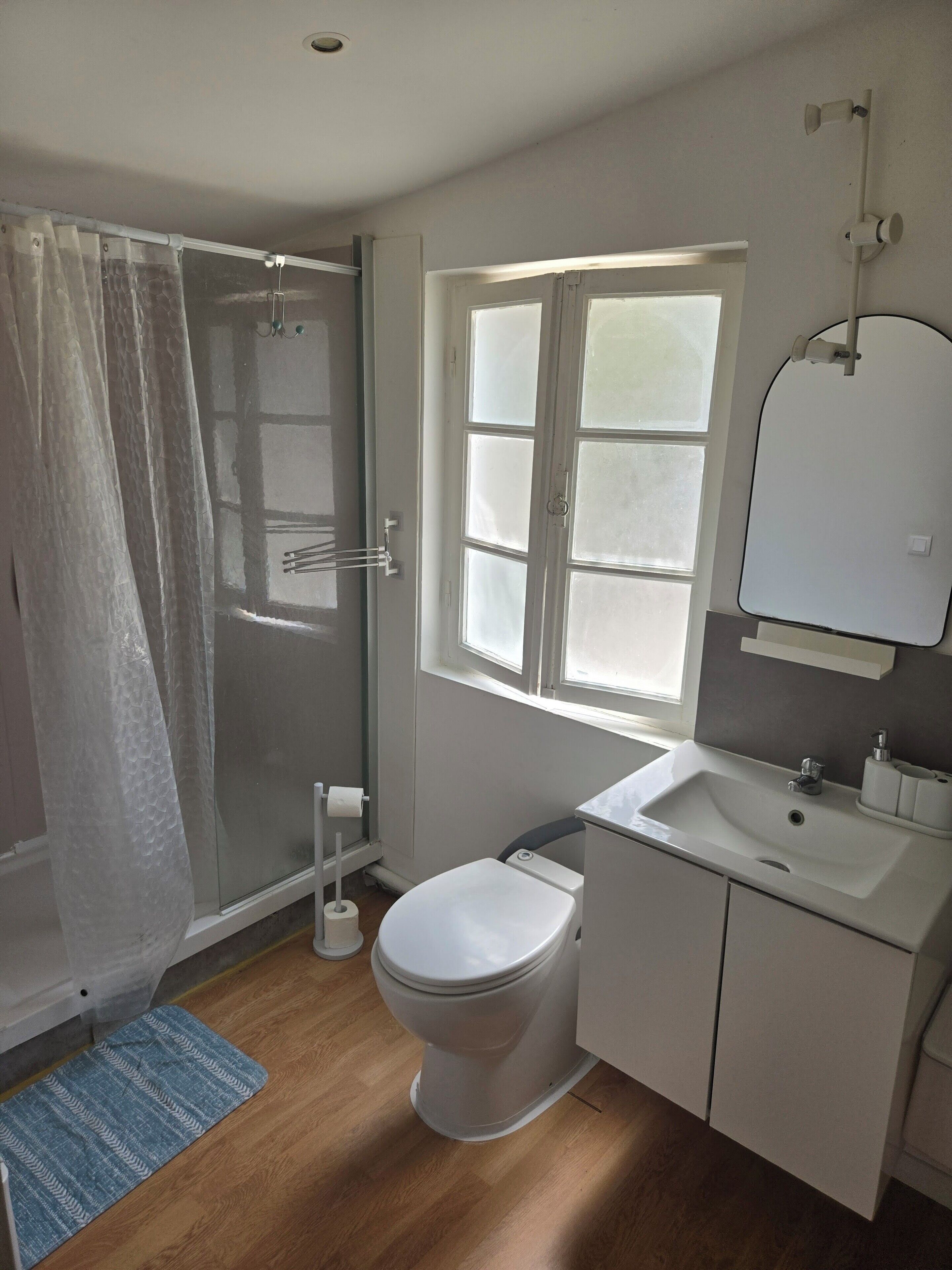 Ein Badezimmer mit Dusche, Toilette, Waschbecken und Fenster.
