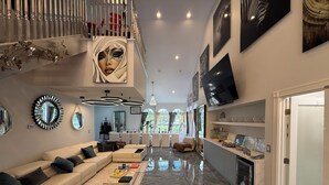 Ein großzügiger Wohnbereich mit hohen Decken, einer Treppe und einem großen Wandfernseher.