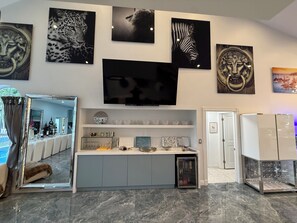 A modern kitchen with a built-in TV, a glass-fronted refrigerator, and a marble countertop. - Luxury 6 Bedroom Pool Home, Sleeps 14, Water Access and Kayaks (Wilton Manors)