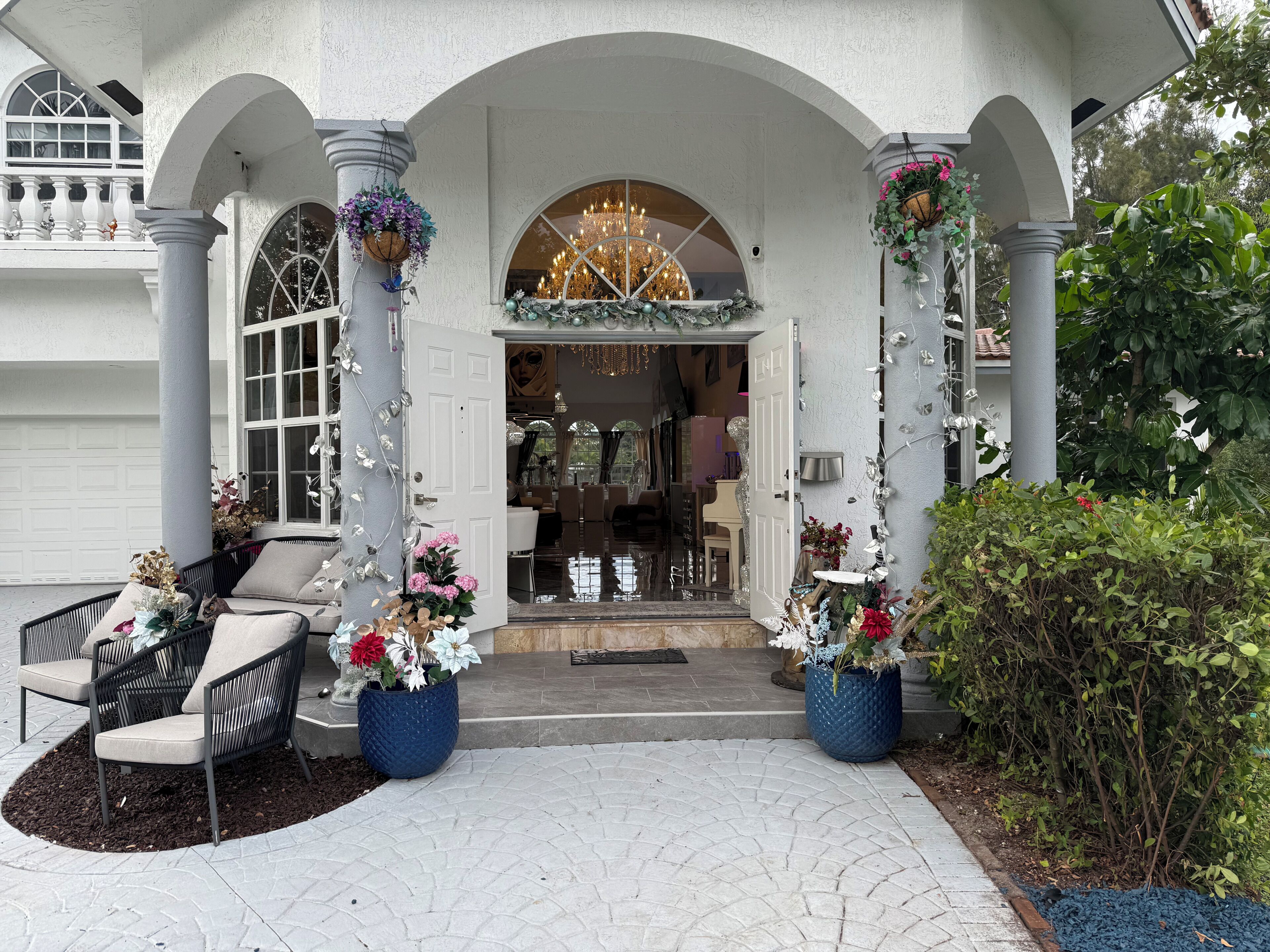 A grand entrance with a chandelier, white columns, and potted plants.