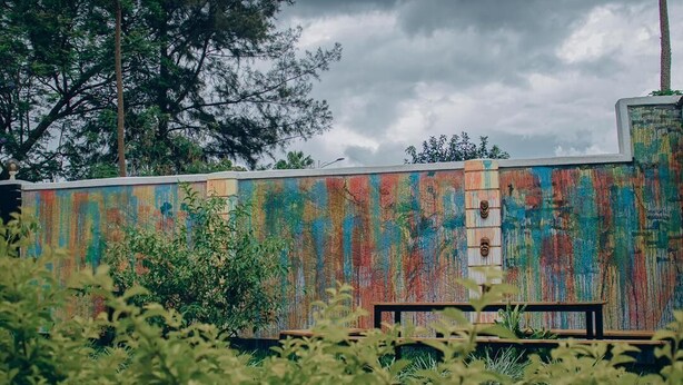 Un edificio con una pared exterior colorida, una banca y algo de vegetación en primer plano.