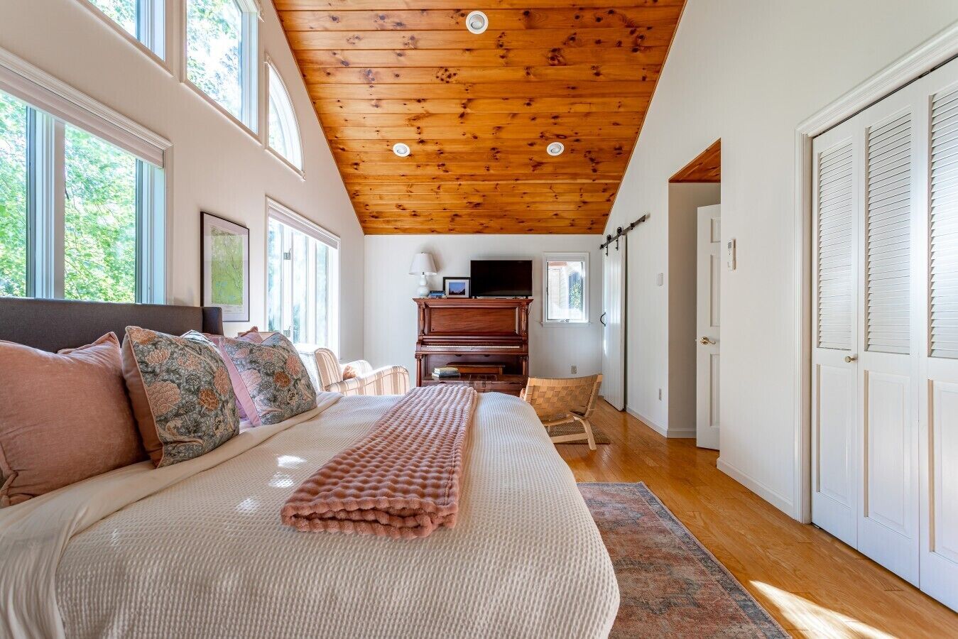 A bedroom with a large bed, a wooden ceiling, a television, and a piano.