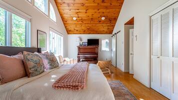 A bedroom with a large bed, a wooden ceiling, a television, and a piano.