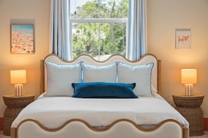 Ein Bett mit geschwungenem Kopfteil, zwei Nachttischlampen und ein Fenster mit Vorhängen.