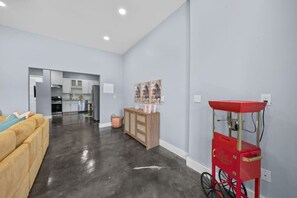 A modern living room with a sofa, a kitchen in the background, and a red cart with a bicycle. - Huge Game Room & Backyard | 10 min walk to Beach (Santa Rosa Beach)