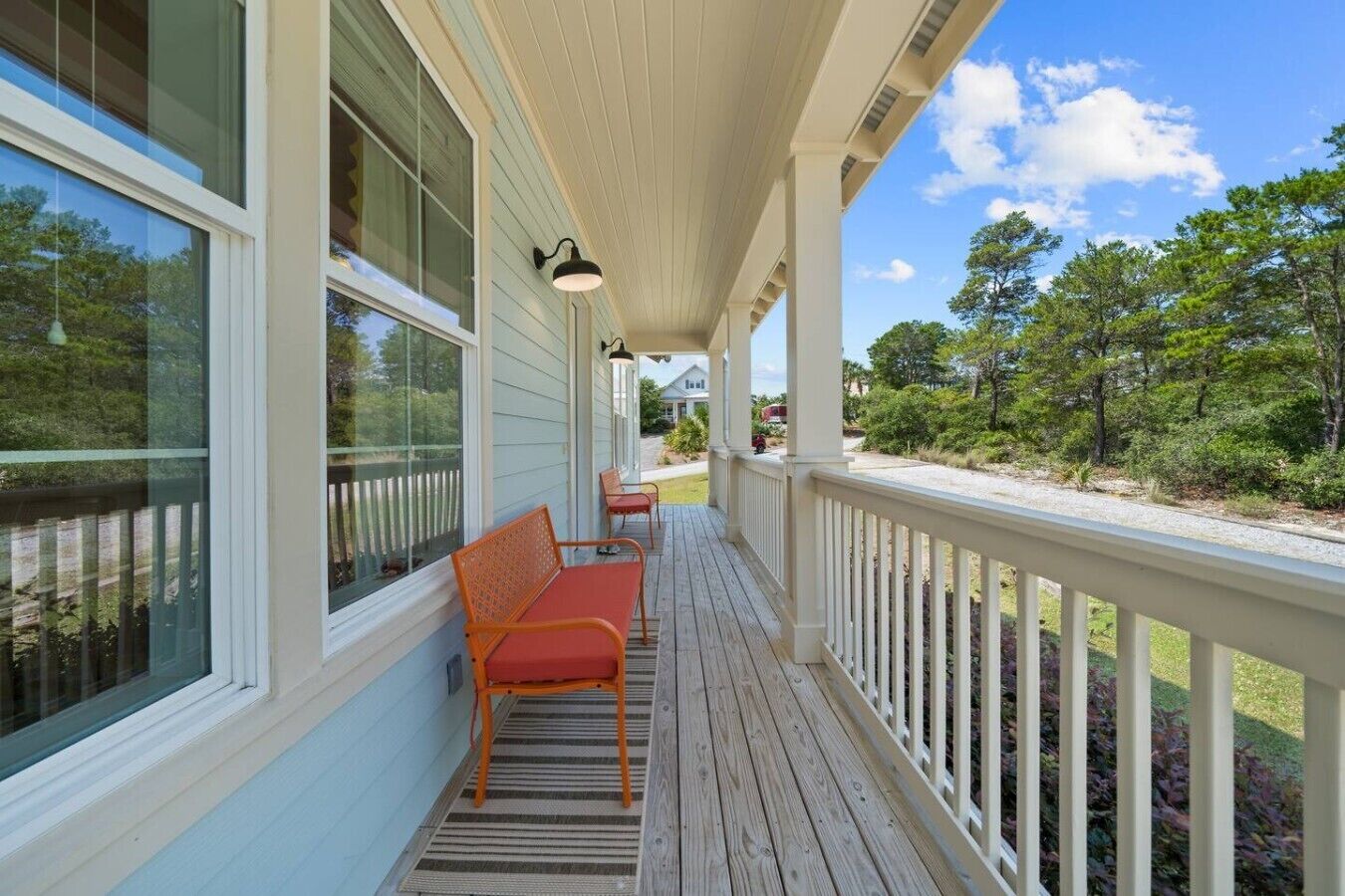 A covered porch with two chairs, a railing, and a view of the surrounding greenery.