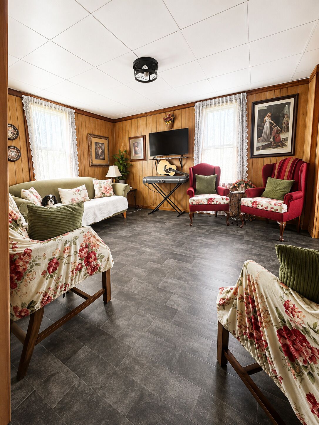 Ein gemütliches Wohnzimmer mit einer Couch, Sesseln, einem Fernseher und einer Gitarre.