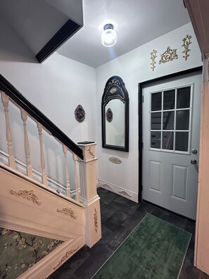 A staircase with a white handrail and a black balustrade, a wall-mounted mirror with an ornate frame, and a door with a window.
