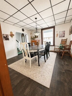 A dining area with a marble table, black and white chairs, a hanging light fixture, and a patterned rug.