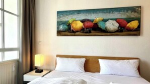 A hotel room with a bed, a nightstand with a lamp, and a painting of colorful umbrellas on the wall. - Urlaub in Sellin Nahe Seebrucke (Sellin)