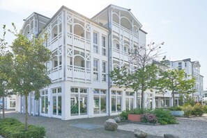 A white multi-story building with balconies, large windows, and a paved courtyard with plants and rocks. - Urlaub in Sellin Nahe Seebrucke (Sellin)