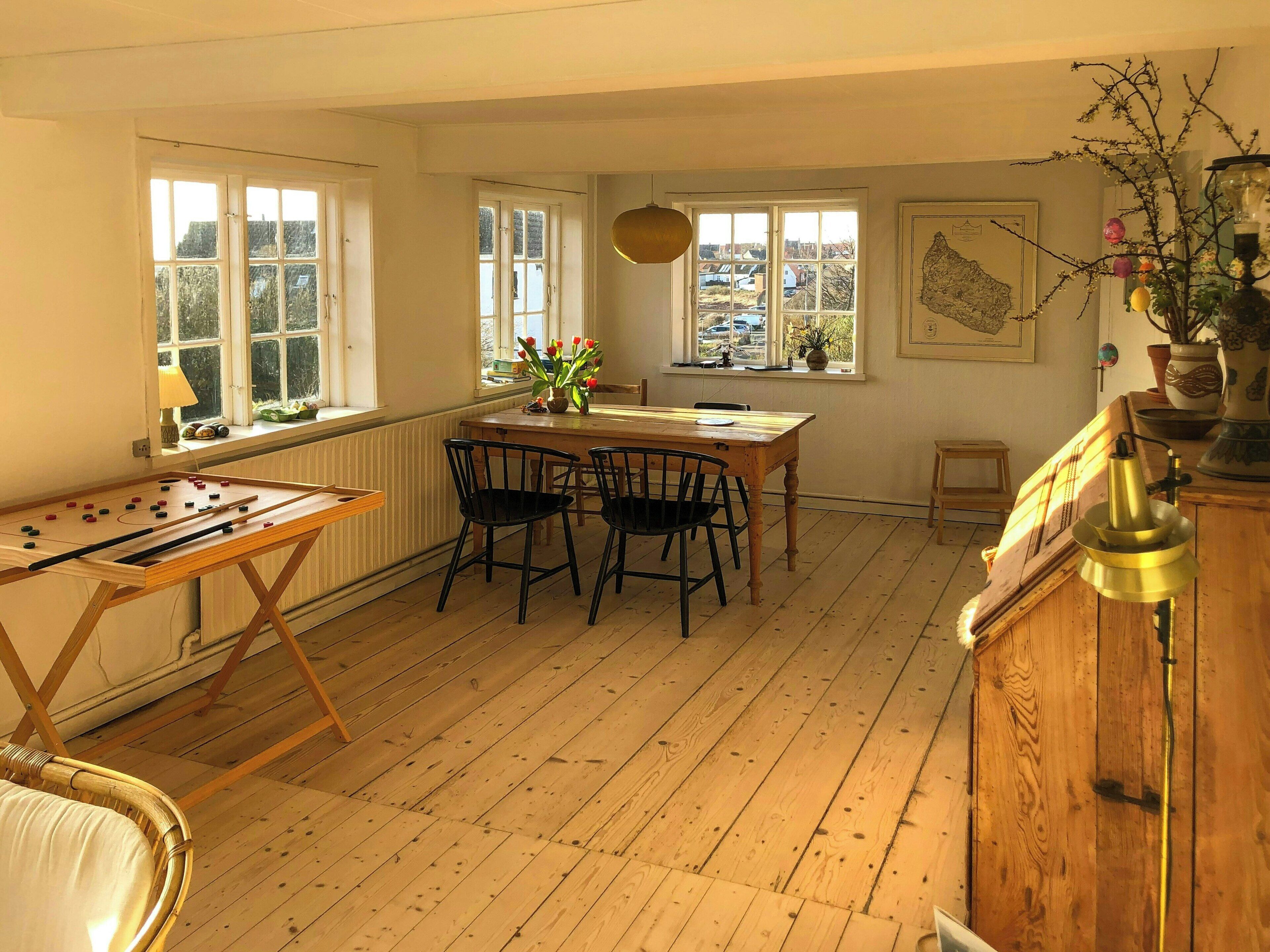 A room with a wooden table, chairs, a foosball table, windows, a radiator, and a map on the wall.
