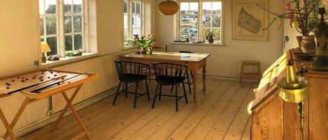 A room with a wooden table, chairs, a foosball table, windows, a radiator, and a map on the wall.
