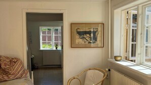 Une pièce comprenant un lit, deux fauteuils en osier, une petite table, une fenêtre donnant sur un paysage agréable et un tableau encadré accroché au mur.