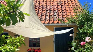 Une cour avec une table et des chaises, un auvent suspendu, une jardinière et un toit recouvert de tuiles.