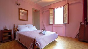 Ein Schlafzimmer mit einem Bett, einem Nachttisch, einer Kommode, einem Spiegel und einem Fenster mit Fensterläden.
