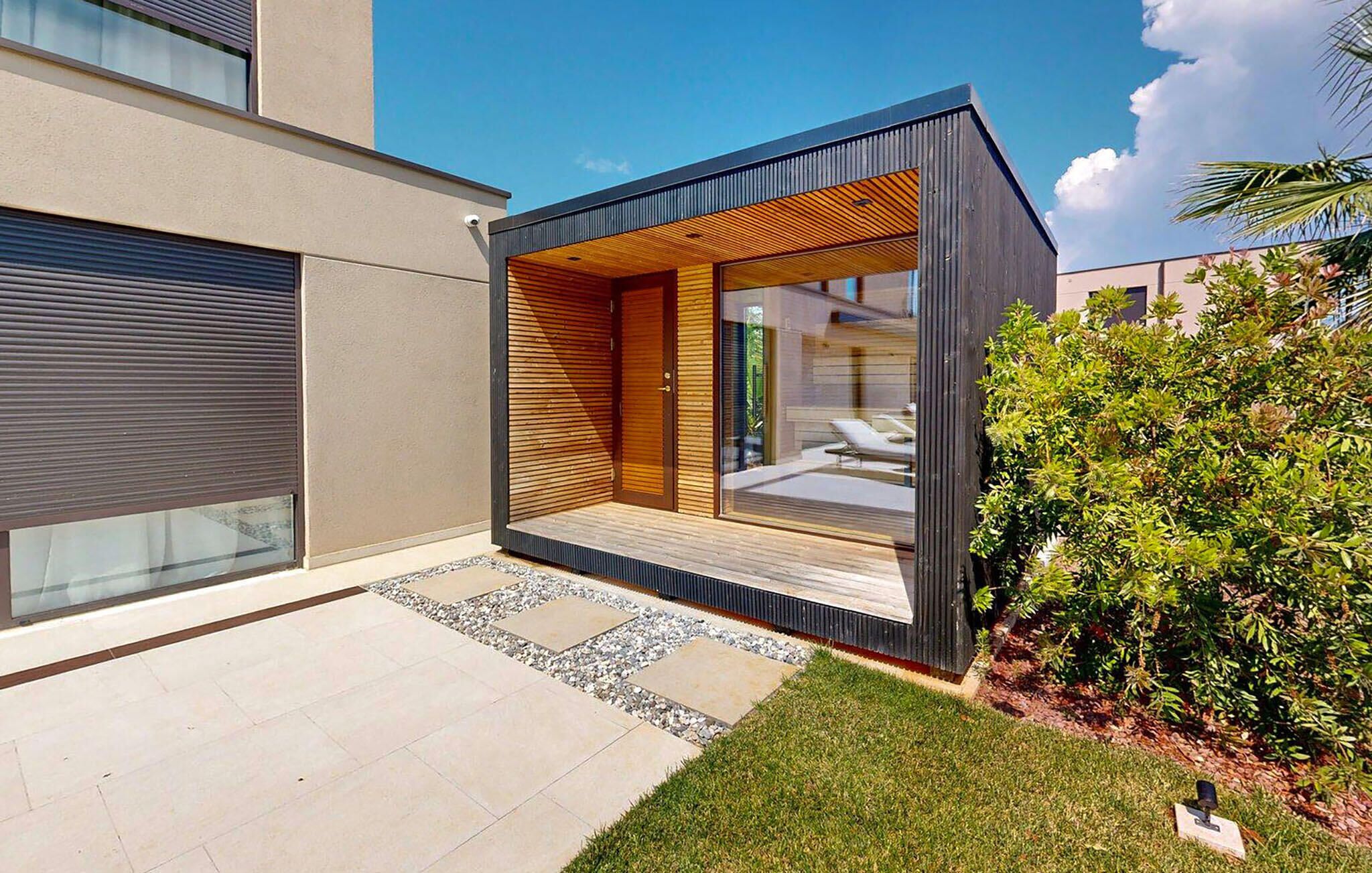 A modern building with a large glass window, a wooden deck, and a well-maintained lawn.