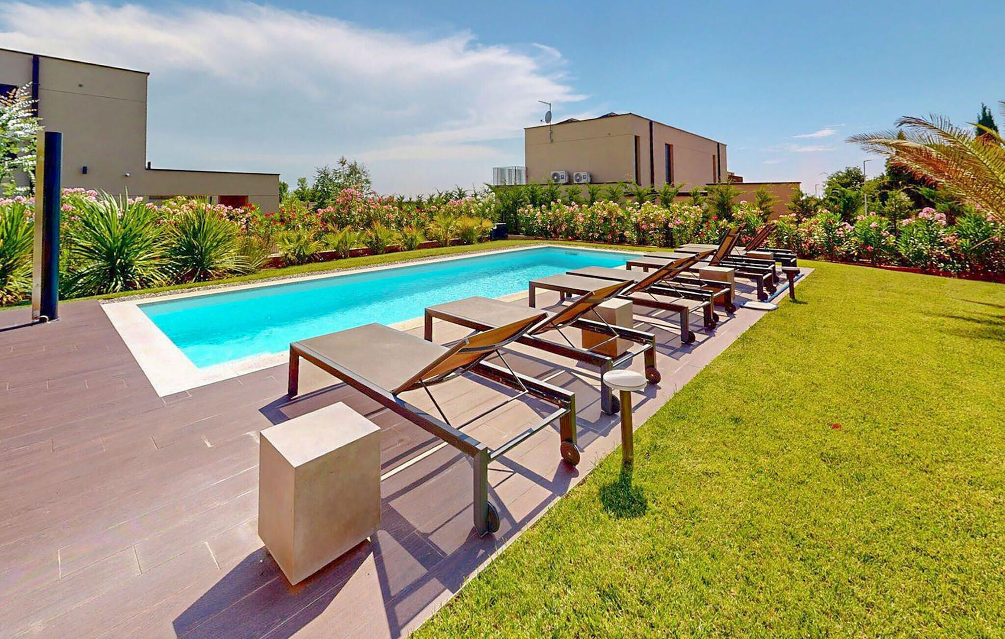 Ein Pool mit Liegestühlen und einer Rasenfläche, umgeben von modernen Gebäuden und gepflegter Bepflanzung.