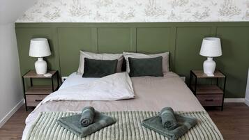 A bedroom with a green headboard, two bedside tables with lamps, a bed with a green blanket, and a patterned wallpaper.