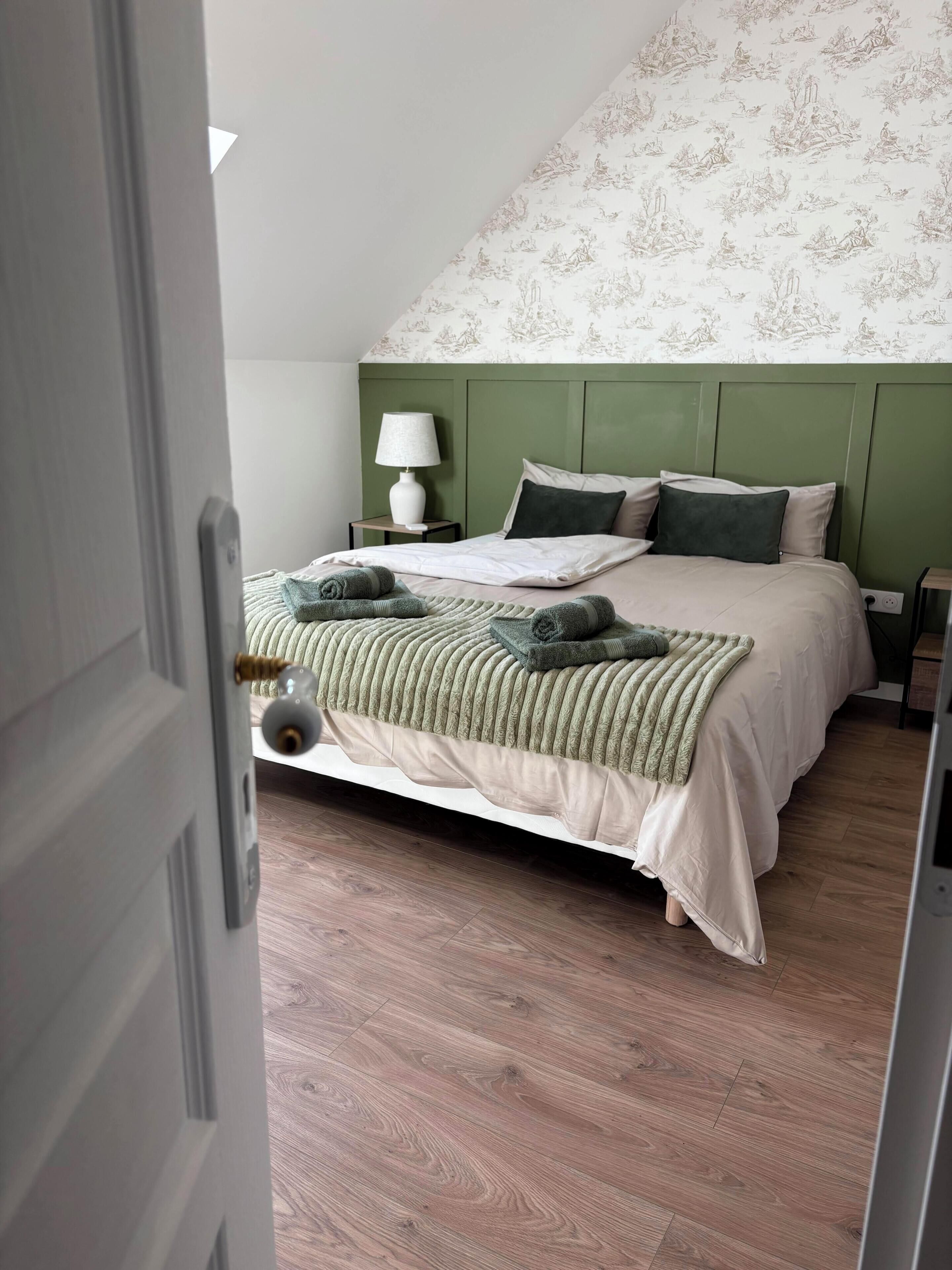 A neatly made bed with pillows and a blanket, a bedside lamp, and a patterned wallpaper.