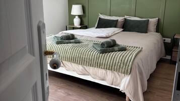 A neatly made bed with pillows and a blanket, a bedside lamp, and a patterned wallpaper.
