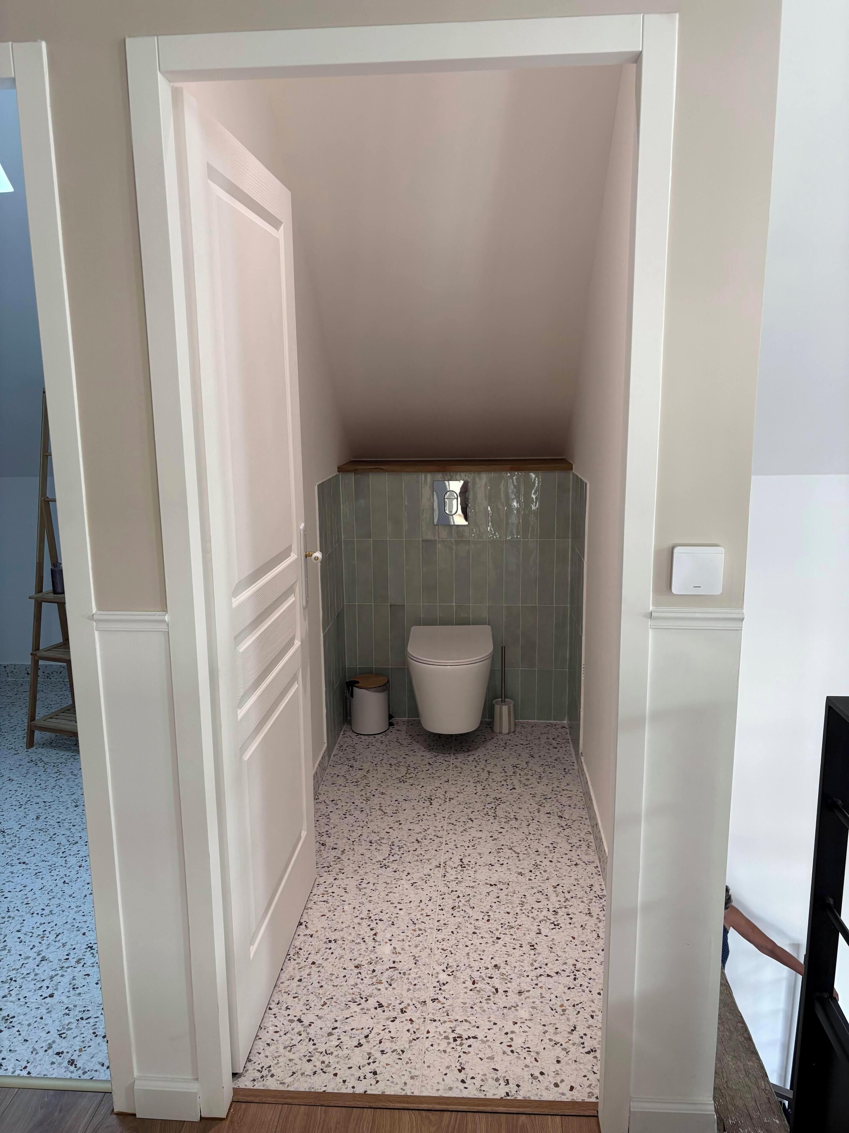 Een compacte, afgesloten badkamer met een toilet, een prullenbak en een schoonmaakborstel.