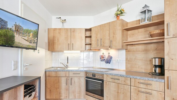 A modern kitchen with wooden cabinets, a built-in oven, and a granite countertop. - Urlaub auf Rugen: Komfortwohnung mit Fitnessraum (Sellin)