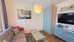 A living room with a sofa, a table, a TV, and a bookshelf. - Urlaub auf Rugen: Komfortwohnung mit Fitnessraum (Sellin)