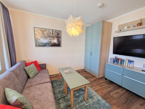 A living room with a sofa, a table, a TV, and a bookshelf. - Urlaub auf Rugen: Komfortwohnung mit Fitnessraum (Sellin)