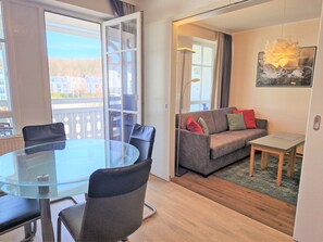 A modern living area with a glass table, leather chairs, a grey sofa, and a small table. - Urlaub auf Rugen: Komfortwohnung mit Fitnessraum (Sellin)
