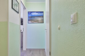 Ein Korridor mit einem gerahmten Bild von einer Strandansicht, einem Lichtschalter und einer Tür zu einem anderen Raum.