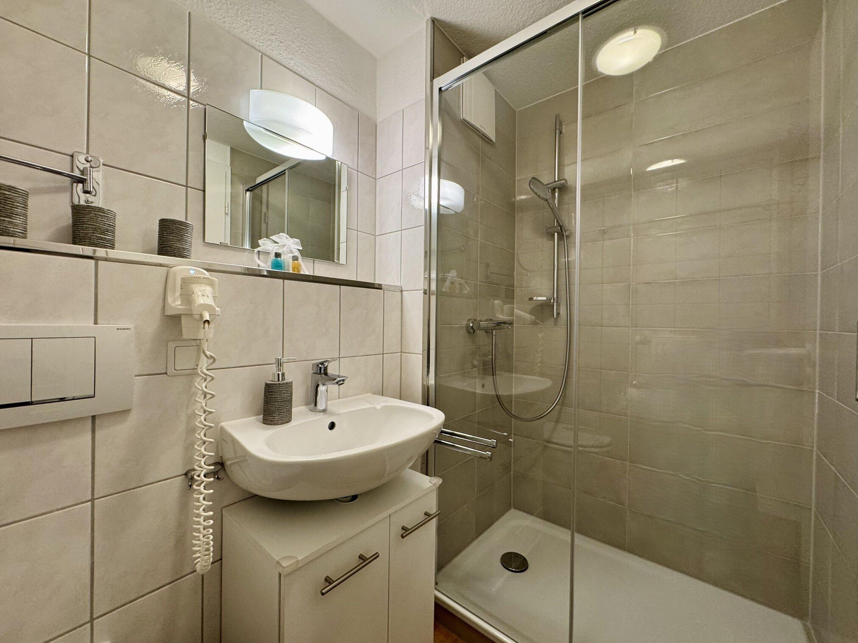 Een moderne badkamer met een douchecabine van glas, een wit wastafelmeubel en een spiegel erboven.