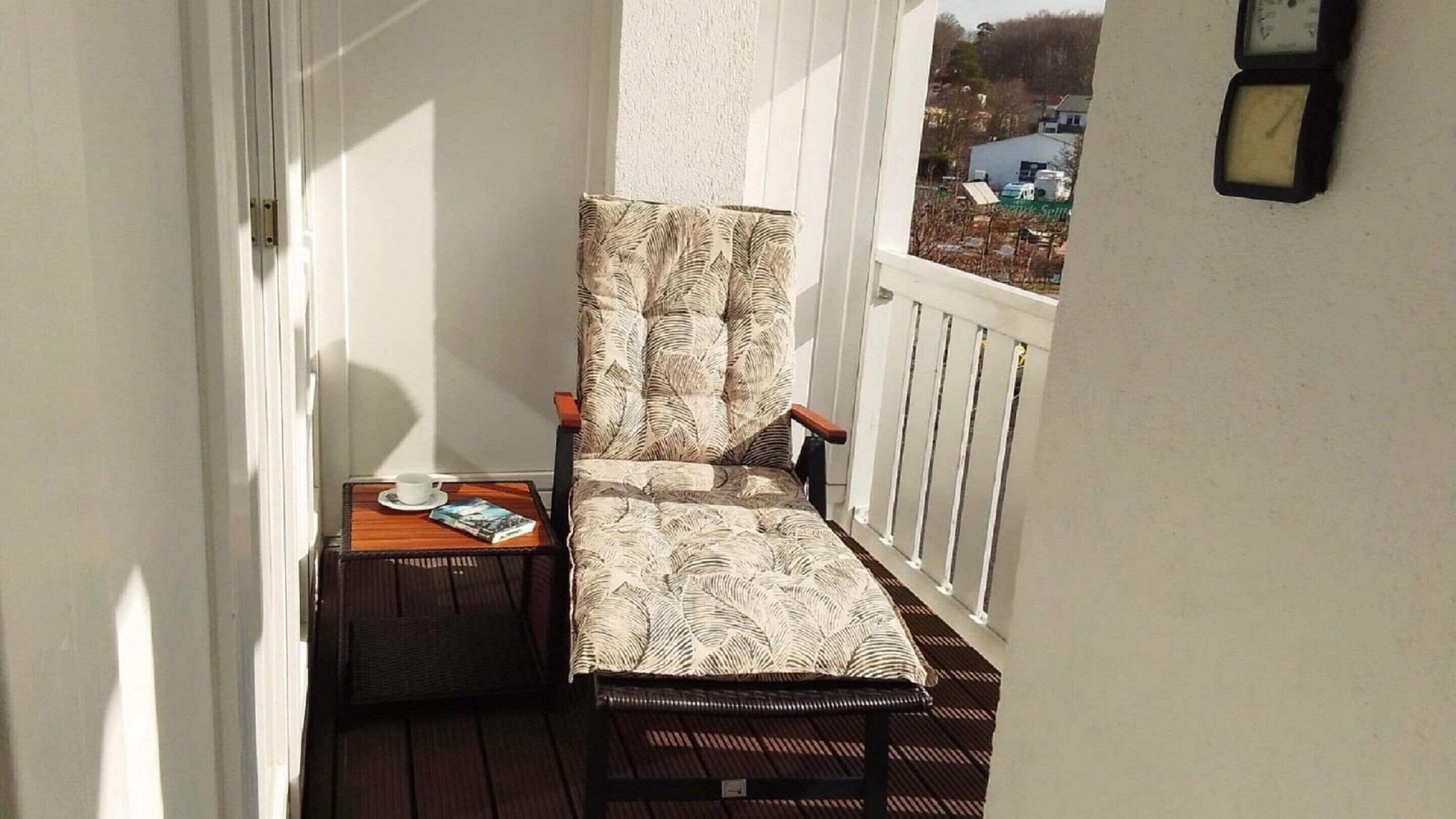 A balcony with a chair, a small table with a cup and book, and a clock on the wall.