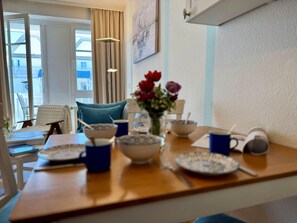 Ein Essbereich mit einem für das Frühstück gedeckten Tisch, einer Blumenvase und Blick ins Freie.