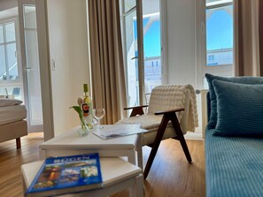 A hotel room with a sofa, a chair, a small table with a bottle and glass, and a book. - Gemutliche Ferienwohnung mit Grossem Balkon in Sellin (Sellin)