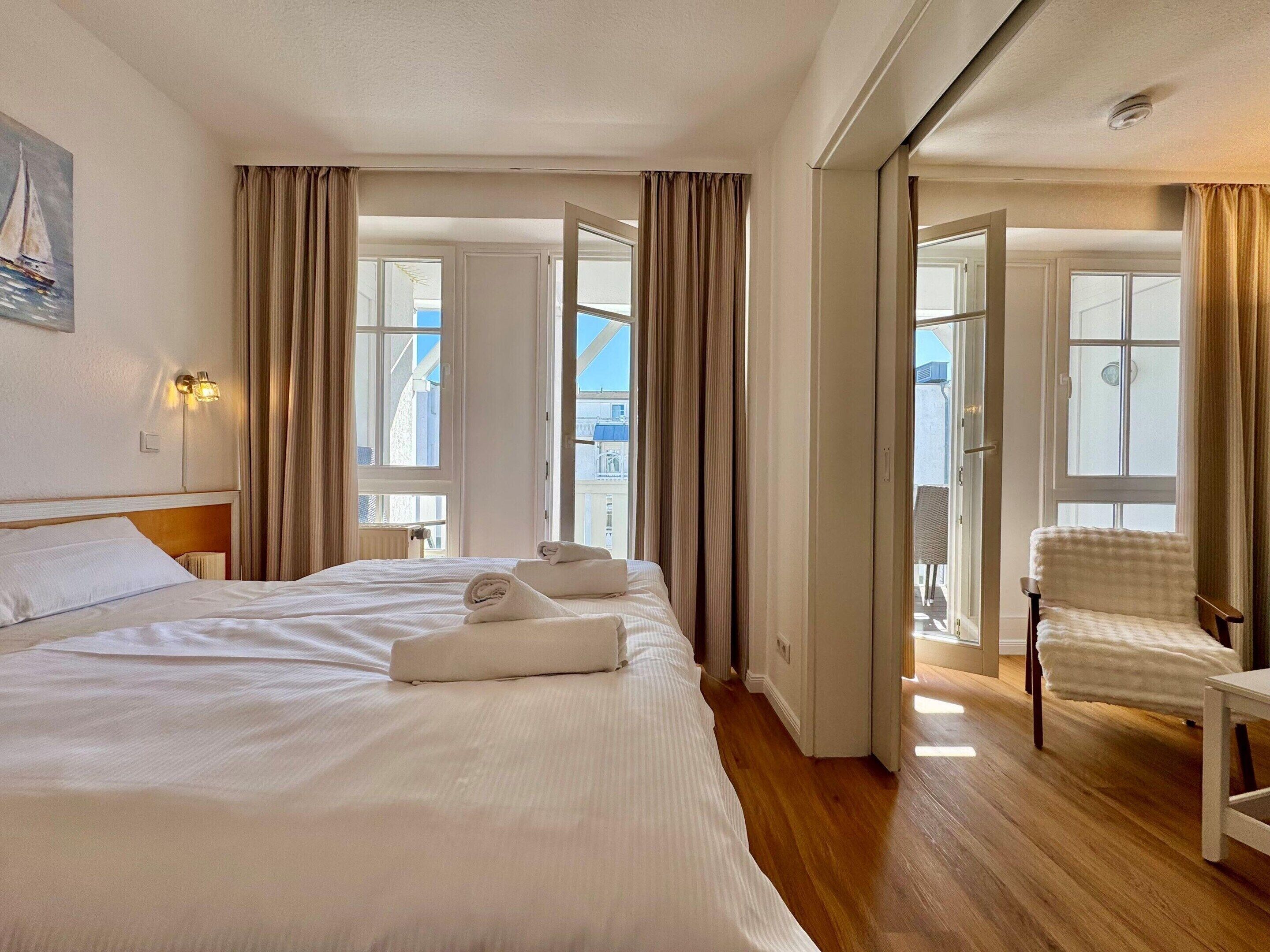 Ein Hotelzimmer mit einem großen Bett, einem Sessel und Blick ins Freie.