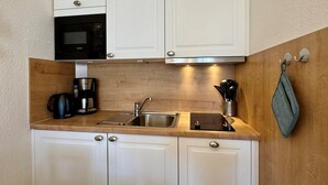 A compact kitchen with white cabinets, a built-in microwave, a coffee maker, and a sink. - Gemutliche Ferienwohnung mit Grossem Balkon in Sellin (Sellin)