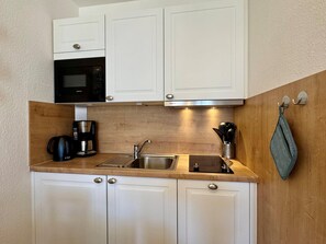 Eine kleine Küche mit weißen Schränken, einer eingebauten Mikrowelle, einer Kaffeemaschine und einem Spülbecken.