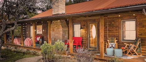 Una cabaña de troncos con chimenea de piedra, porche de madera y zona de estar al aire libre.