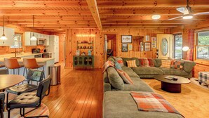 A cabin interior with a dining area, kitchen, and a cozy living room with a sofa and coffee table. - The Oak & Oar Camphouse | Family Lake Retreat (Logan)