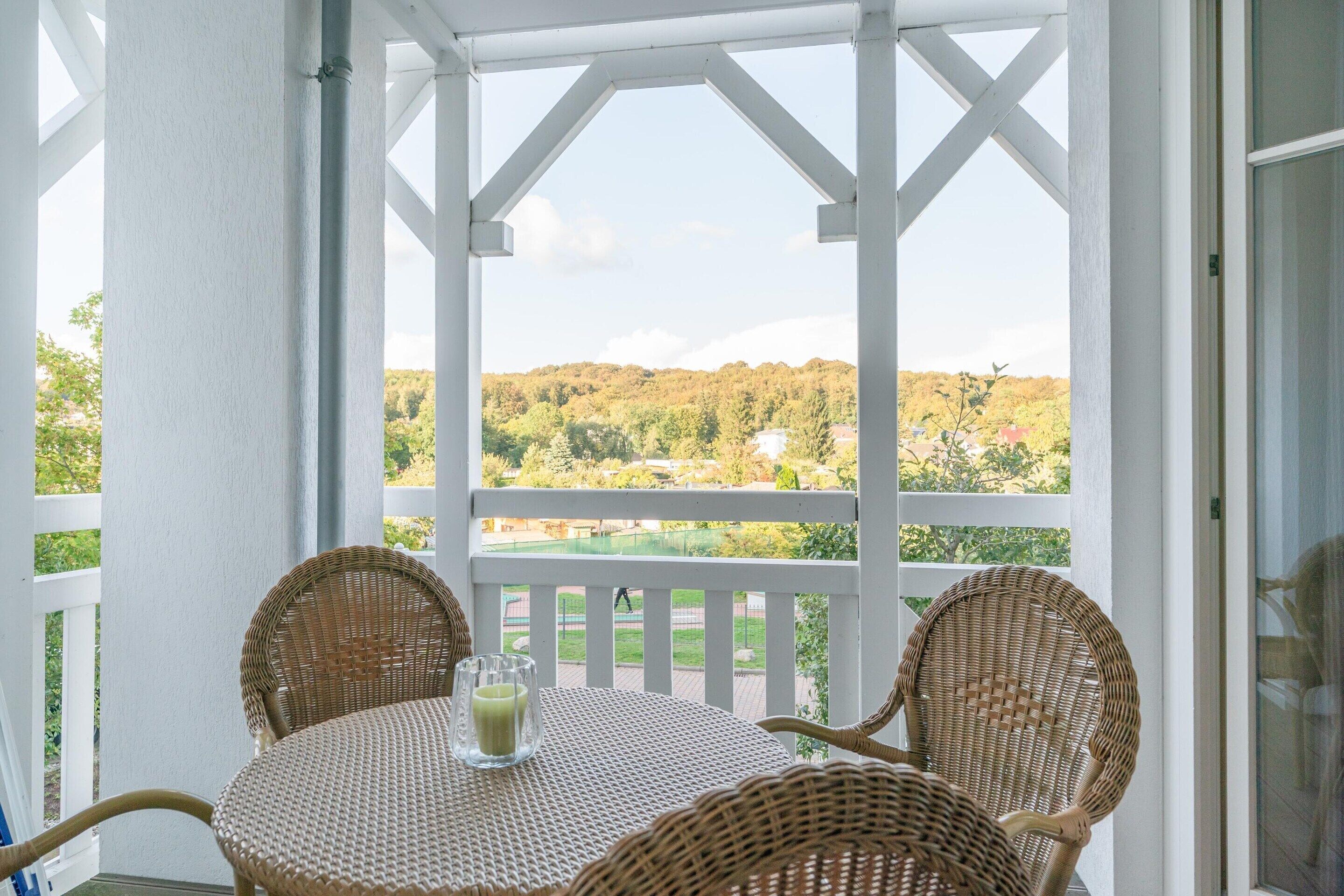 A covered outdoor seating area with wicker chairs and a table, overlooking a green landscape.