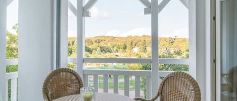 A covered outdoor seating area with wicker chairs and a table, overlooking a green landscape.