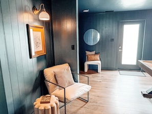 Une pièce avec une chaise, un tableau encadré, un miroir rond et une porte donnant sur une vue agréable.