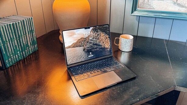 A laptop on a wooden table with a lamp and books.