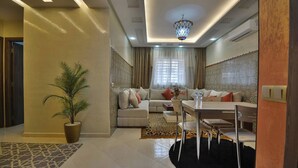 Ein modernes Wohnzimmer mit Sofa, Esstisch, Stühlen, einem Blumentopf und einem gemusterten Teppich.