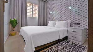 Ein modernes Schlafzimmer mit Bett, Nachttischen, einer Topfpflanze und Wandfliesen mit Muster.