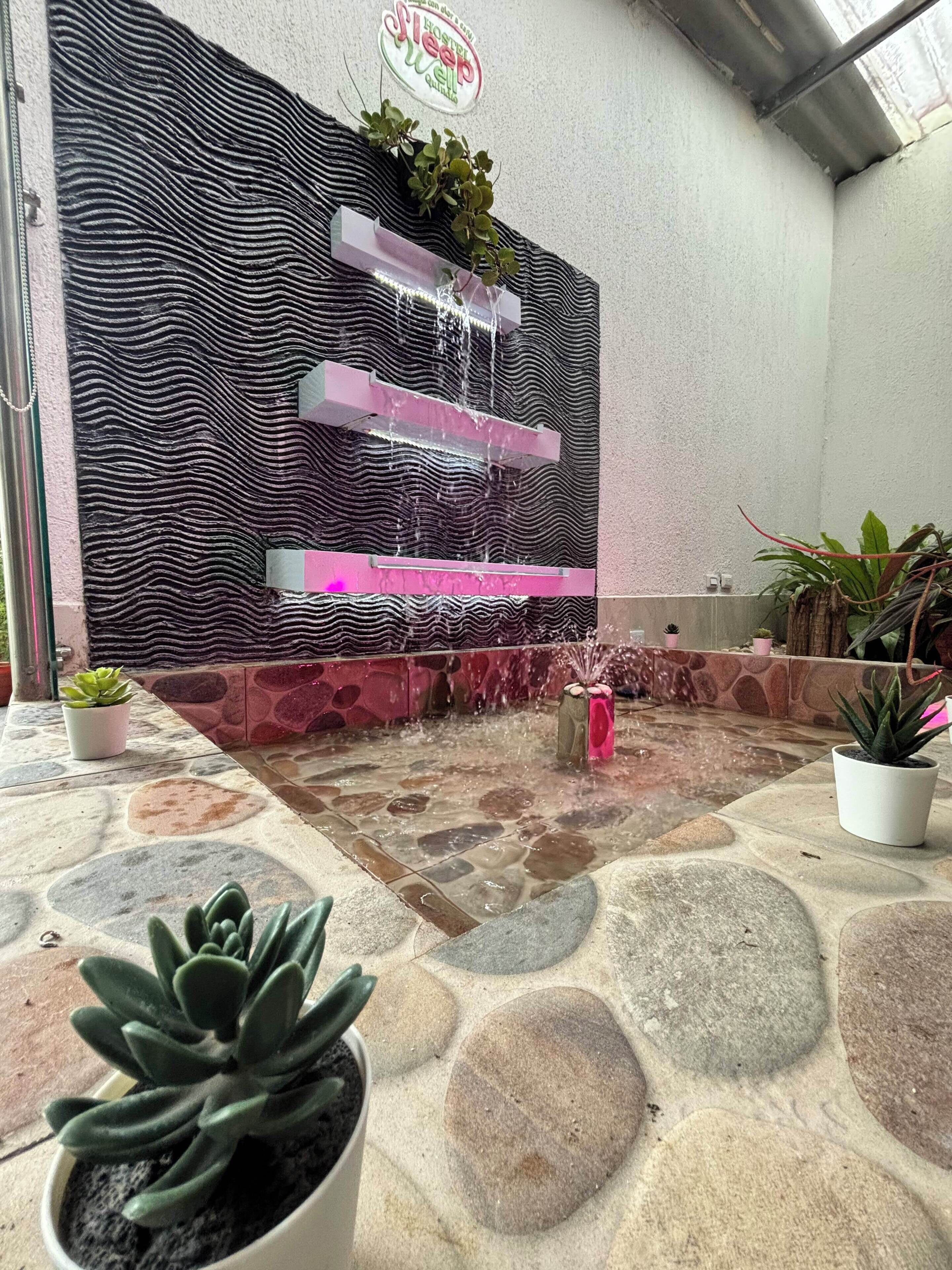 A stone-tiled patio with a water feature, potted plants, and a textured wall.