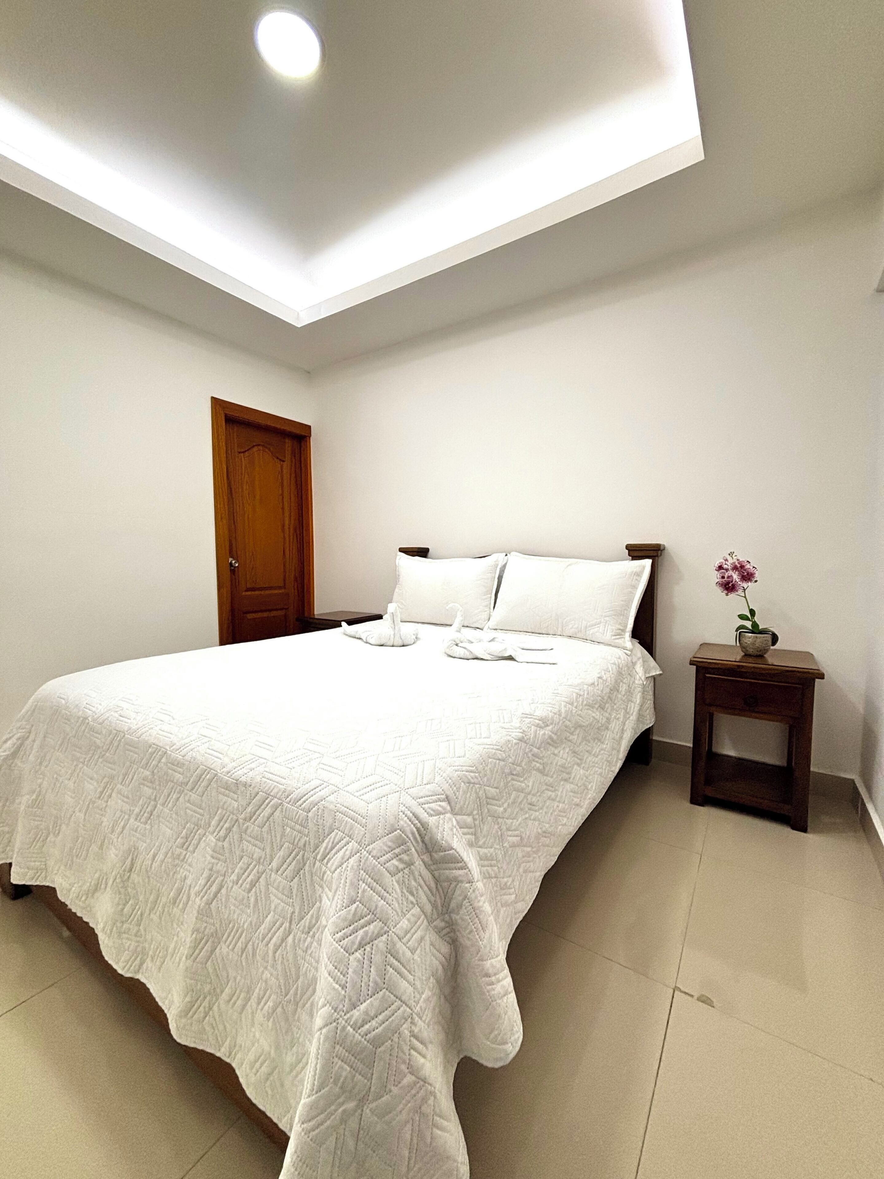 Un dormitorio con cama, mesita de noche, puerta y lámpara de techo.