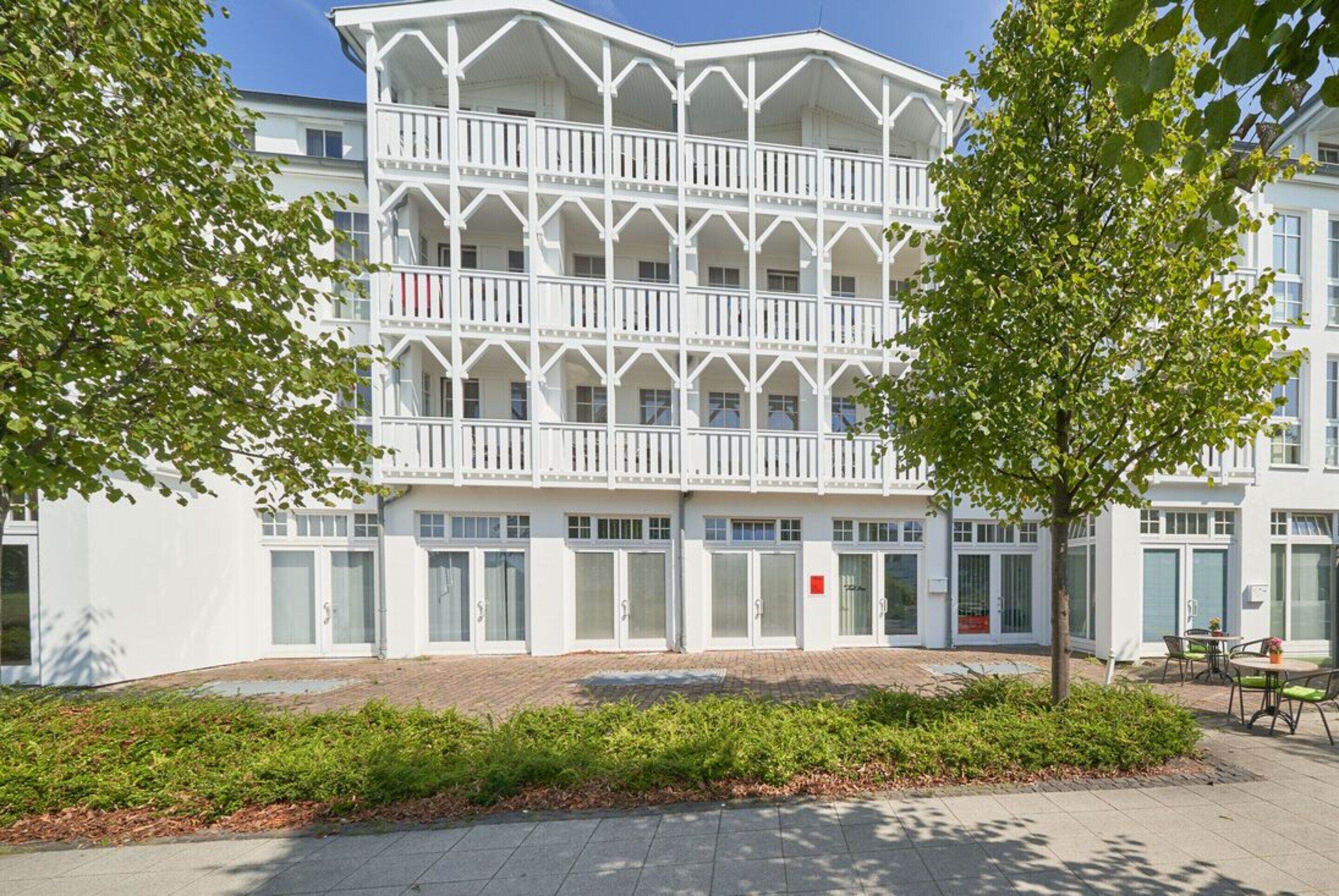 Ein weißes Gebäude mit einer symmetrischen Fassade, mehreren Balkonen und einem gepflasterten Innenhof.