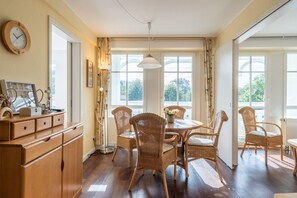 A dining room with wicker chairs, a wooden cabinet, and a large window with curtains. - Ferienwohnung im 1.og mit Balkon in Sellin (Sellin)